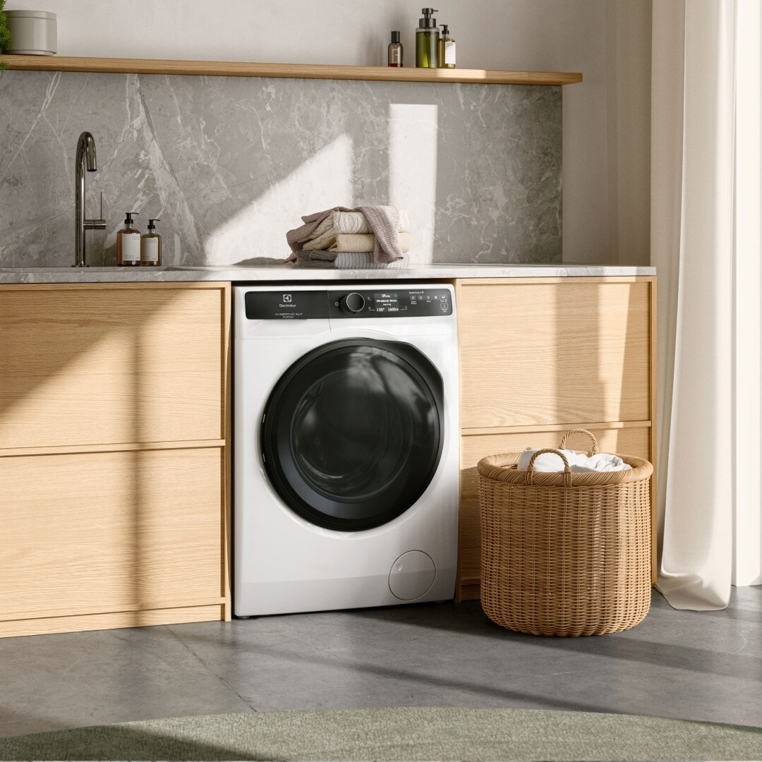 Et lyst vaskerum med en vaskemaskine under et arbejdsbord.